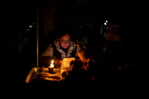 A woman and the top of a table in front of her are dimly lit with a glowing candle.