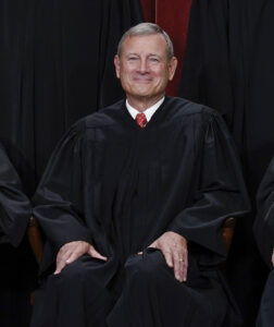 A man in a black court robe sits in a chair.