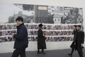 People walking past wall with photos of 240 hostages.