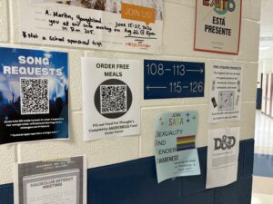 Photo of wall inside Rockbridge County High School, covered with flyers announcing various events and student group recruiting messages, many with QR codes for use by cell phones. 