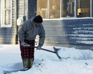 Photo of a man shoveling the snow off the sidewalk leading to his house.