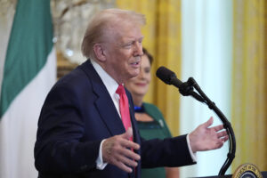 President Trump speaks at a podium in front of Irish flag.