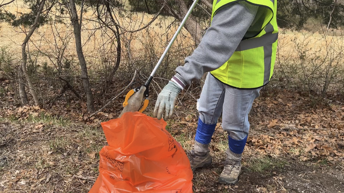 A volunteer picks up trash on the side of the road.