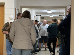 A group of people stand talking in a hallway outside city council executive session. All adults in various outfits.