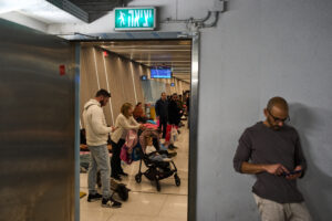 From a stairwell looks into a room, Man up close on phone and families and more people behind him. All underground waiting around