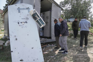 Four people in the right of the frame looking at a damaged building. Part of it to the left in disrepair. 