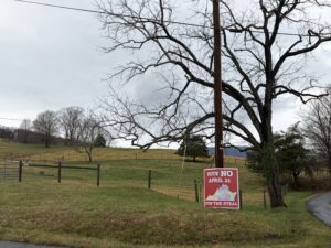 Green field, gray skies, tree, and fence. Sign to vote no in the election. 